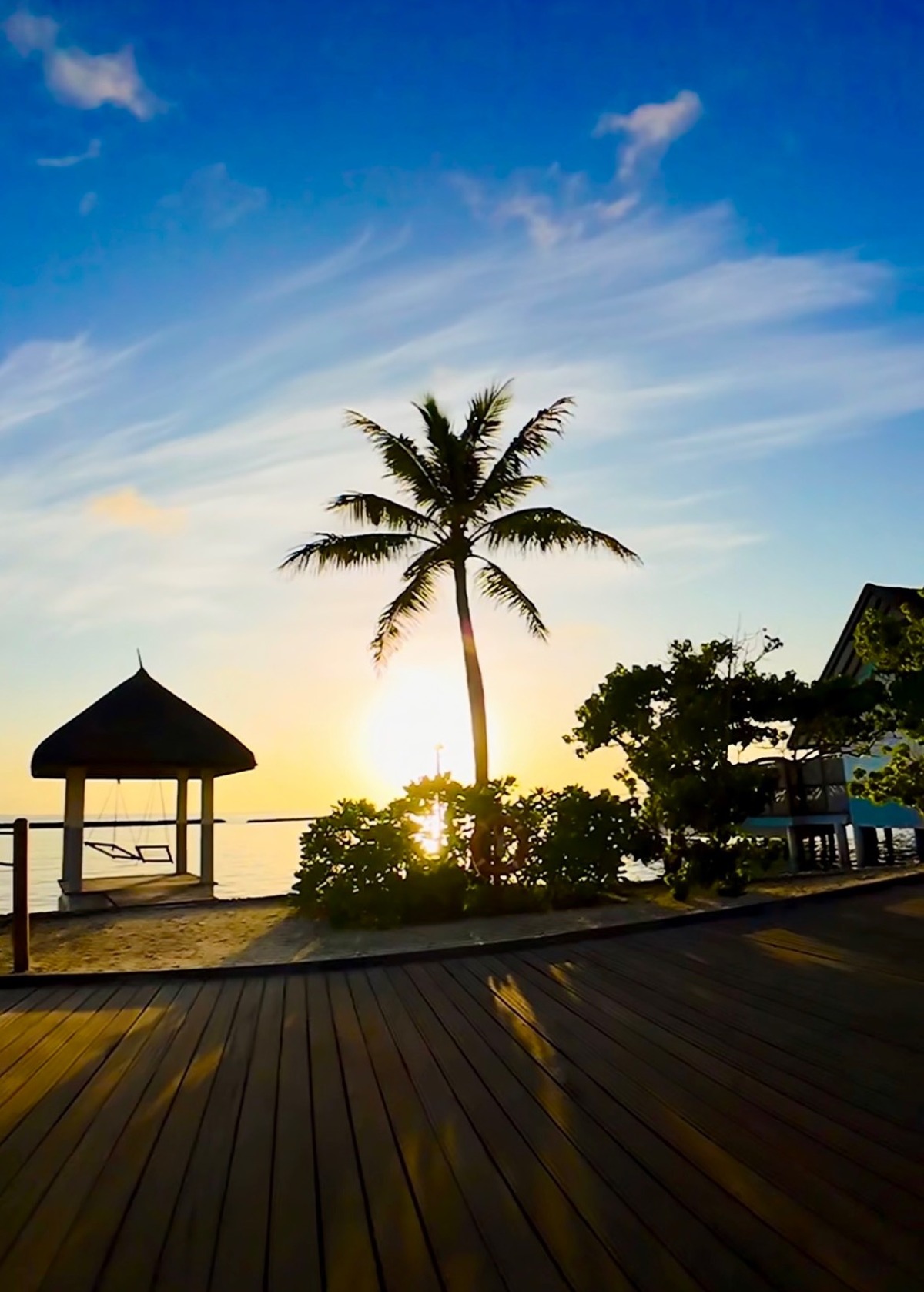 Sunset over a tropical island boardwalk with a palm tree, pavilion and the sea
